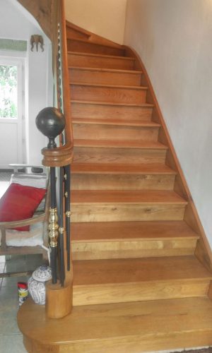 Escalier en chêne massif sur noyau et sur 2 étages ; départ avec volute; poteau et balustre en acier noir avec bague laiton.