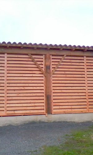 Hangar garage en douglas massif avec ferme moisée sur poteau et mur persienné.