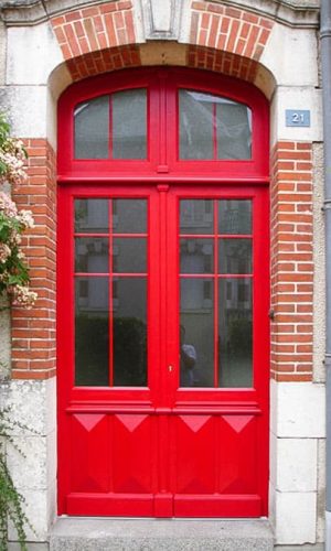 Menuiserie porte d'entrée en chêne massif brun peint en rouge ; imposte fixe de forme anse de panier ; panneau bas en pointe de diamant.